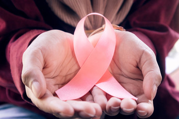 Woman's hand holding a pink ribbon.Concept: Breast Cancer Awareness.