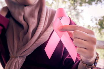 Woman's hand holding a pink ribbon.Concept: Breast Cancer Awareness.