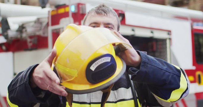 Close up portrait of fireman in helmet and gull equipment standing next to the car. Rescuer takes off helmet and smiles looking at camera. Concept of saving lives, heroic profession, fire safety