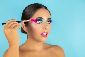 Fototapeta premium Beauty portrait of female model with vivid makeup and brush on blue background.