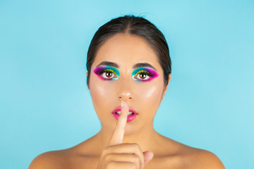 Beauty portrait of female model with vivid makeup on blue background.
