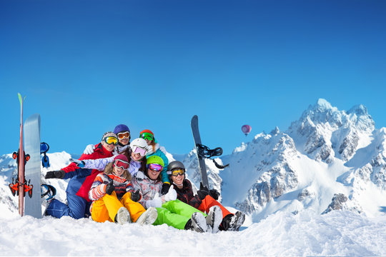 Large group of happy young adults lay in snow wave hands with snowboards and ski over mountain peaks