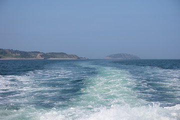 Wake from a motorboat sailing along the menai strait at anglesey. Puffin island and the coast with blue sea and a summer sky.