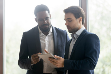 Diverse colleagues or business partners studying electronic document on tablet computer screen, smart caucasian agent offering life insurance, loan or rental of real estate to millenial african client