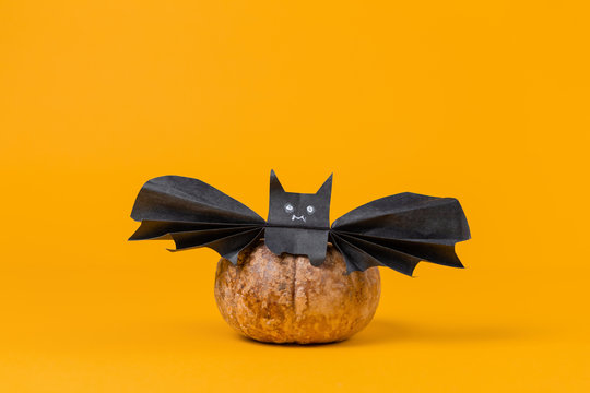 A pumpkin on which a bat is sitting, made of paper. Orange background. Copy space. The concept of Halloween, and holiday decorations