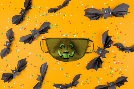 Reusable anti-virus mask with print of jack lantern surrounded by paper bats. Orange background with decorative stars. Flat lay. The concept of protection from the virus during Halloween