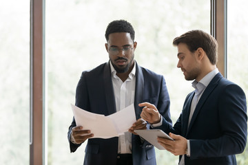 Serious caucasian businessman consulting african colleague about contract details, attentive...