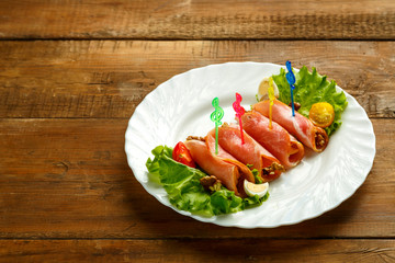 Ham rolls on a plate with green salad near eggs on a wooden table. save a place. horizontal