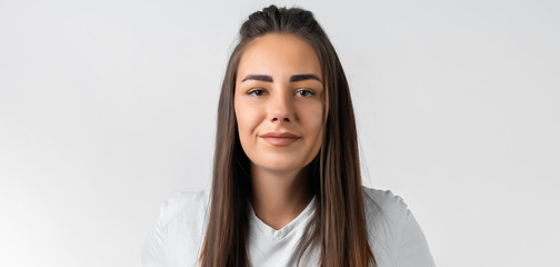 Modern girl with long chestnut hairs in casual light clothes posing isolated on white wall...