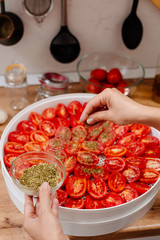 Sun-dried tomatoes. The process of cooking sun-dried tomatoes. The woman is preparing tomatoes in the kitchen. A woman cuts tomatoes, greases them with oil and spices them. 