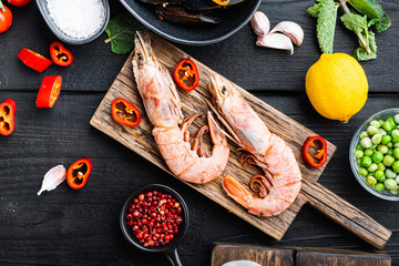 seafood king prawns on wooden board with spices on black wooden background, flat lay