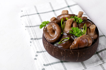 Pickled milk mushrooms with onion and spices topped with parsley in wooden bowl on the white table. Russian cuisine appetizer