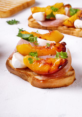 Bruschetta with grilled peaches, prosciutto and mozzarella topped with parsley and cilantro on the white table