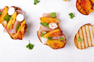 Bruschetta with grilled peaches, prosciutto and mozzarella topped with parsley and cilantro served on the white table. Top view