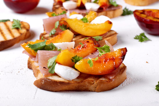 Bruschetta with grilled peaches, prosciutto and mozzarella topped with parsley and cilantro on the white table