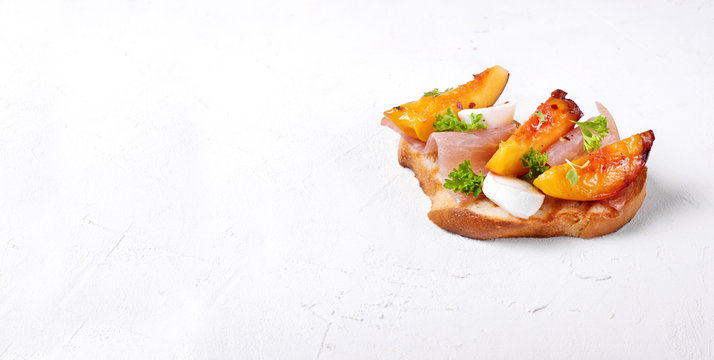 Bruschetta with grilled peaches, prosciutto and mozzarella topped with parsley and cilantro on the white table. Copy space