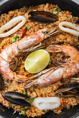 Seafood and chicken paella with rice, mussles, shrimps,chicken, tomatoes and wine in pan on white textured background, flat lay