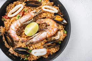 Paella cooked in frying pan on white textured background, flat lay