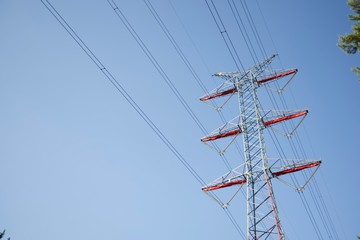 a power mast of a high voltage transmission line against blue sky with sun