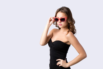 Gorgeous elegant woman wearing black dress in sunglasses posing in the studio on grey.