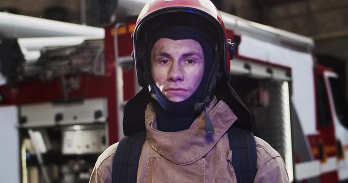 Portrait of caucasian handsome fireman in helmet and gull equipment standing next to the car and looking into camera. The concept of saving lives, heroic profession, fire safety