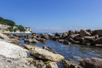 Fototapeta na wymiar Rocky shore with splashing waves and limestone cliff in background at UNESCO site Stevns Klint, Denmark