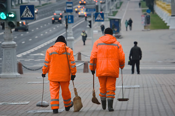 Workers sweeping pavement with broom. Workers walking with broom and scoop in hands andd sweep street. Municipal worker in uniform with broomstick and scoop for garbage, cleaning service