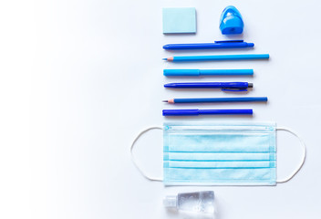 The concept of returning to school in a new format. Blue school supplies, pencils, pens, markers, paper clips, medical mask and sanitizer on a light background. Space for text