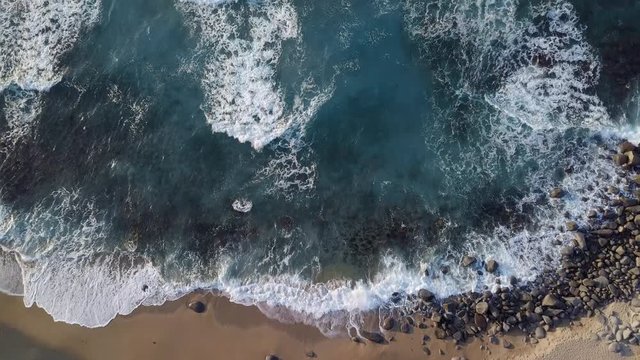 Waves consecutively lapping onto the shore and white bubbles remaining on the surface of beautiful blue ocean.