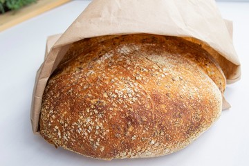 Composition in the rays of the daytime sun. Homemade whole grain rye bread in a craft paper bag. On a light background