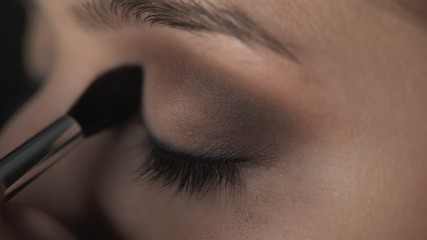 Makeup artist making professional make-up for young woman in beauty studio. Make up Artist uses brush to applies shadow on eyelid