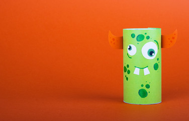 green scary monster made from a roll of toilet paper on orange background