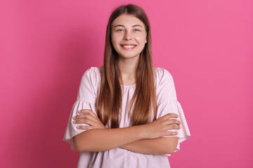 Obraz premium Portrait of nice well dressed attractive lovely girl with folded arms isolated over bright pink background, looking smiling directly at camera, expressing joy.