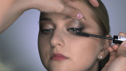 Makeup artist making professional make-up for young woman in beauty studio. Make up Artist uses mascara to make eyelashes