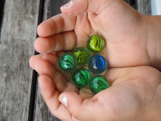 Colored glass balls in the palm of a small child in front of a wooden table