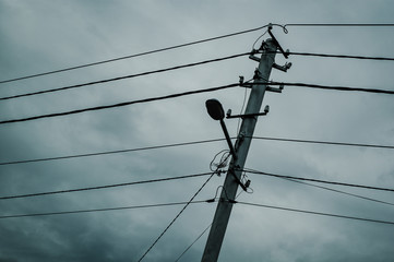 Concrete pole with electricity line cables and a lamp.
