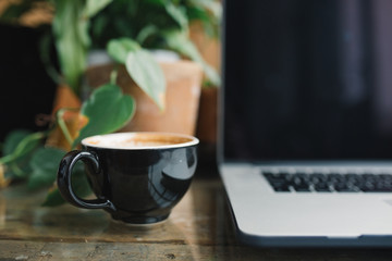 Close up of black cup of coffee, laptop with blank screen and green potted plant on background. Blog, website, social media hero header template.