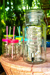 Glass Beverage Drink Dispenser, Glasses with Handle, colored Lids and Straws decorated on a table