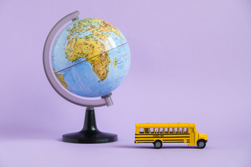 Back to school concept. Traditional yellow school bus and world globe on purple background. Transfer to school. Yellow toy model school bus.