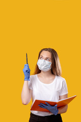 School reopen. Quarantine restriction. Female teacher in protective face mask gloves holding open book isolated on yellow pointing up at copy space. COVID-19 hygiene measures. Announcement background.