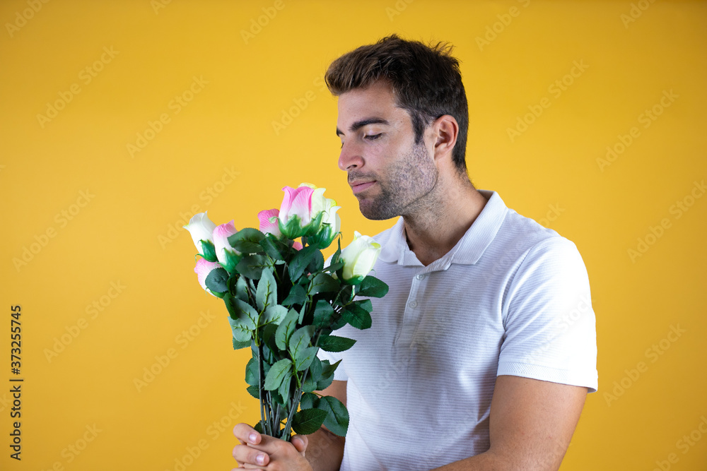 Wall mural young handsome man standing over yellow insolated background with roses