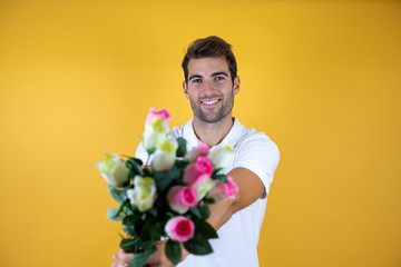 young handsome man standing over yellow insolated background smiling holding flowers © Irene