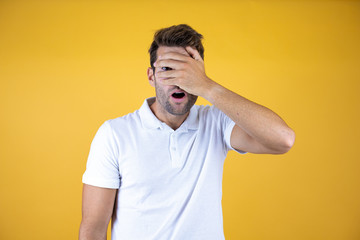 Fototapeta na wymiar Young man standing over isolated yellow background peeking in shock covering face and eyes with hand, looking through fingers with embarrassed expression