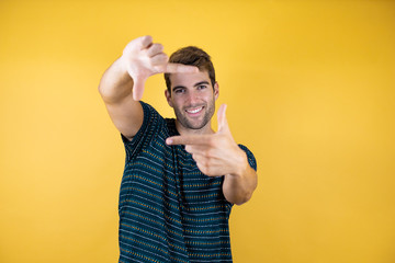 Young handsome man over yellow isolated background doing frame using hands palms and fingers, camera perspective