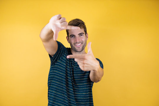 Young handsome man over yellow isolated background doing frame using hands palms and fingers, camera perspective