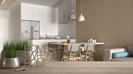 Wooden table, desk or shelf with potted grass plant, house keys and 3D letters home sweet home, over classic kitchen and lounge, architecture interior design, copy space background