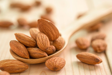 Closeup of brown fresh almonds seed in wooden spoon on wooden table.