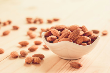 Closeup of brown fresh almonds seed in white bowl on wooden table.