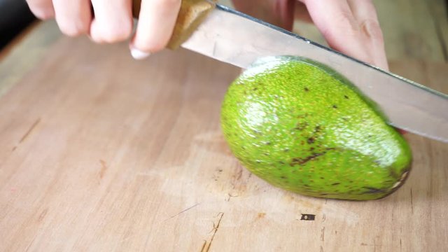 cutting a ripe avocado with a metal knife with a wooden handle