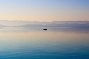 Dawn over the water surface of the lake. Lonely boat with a fisherman. Calm, clear water. Turgoyak, Russia.
